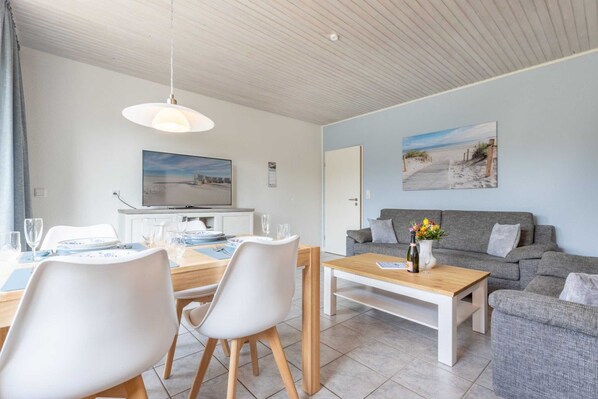 Uma sala de estar moderna com área de jantar, sofás cinza e mesa de centro de madeira.