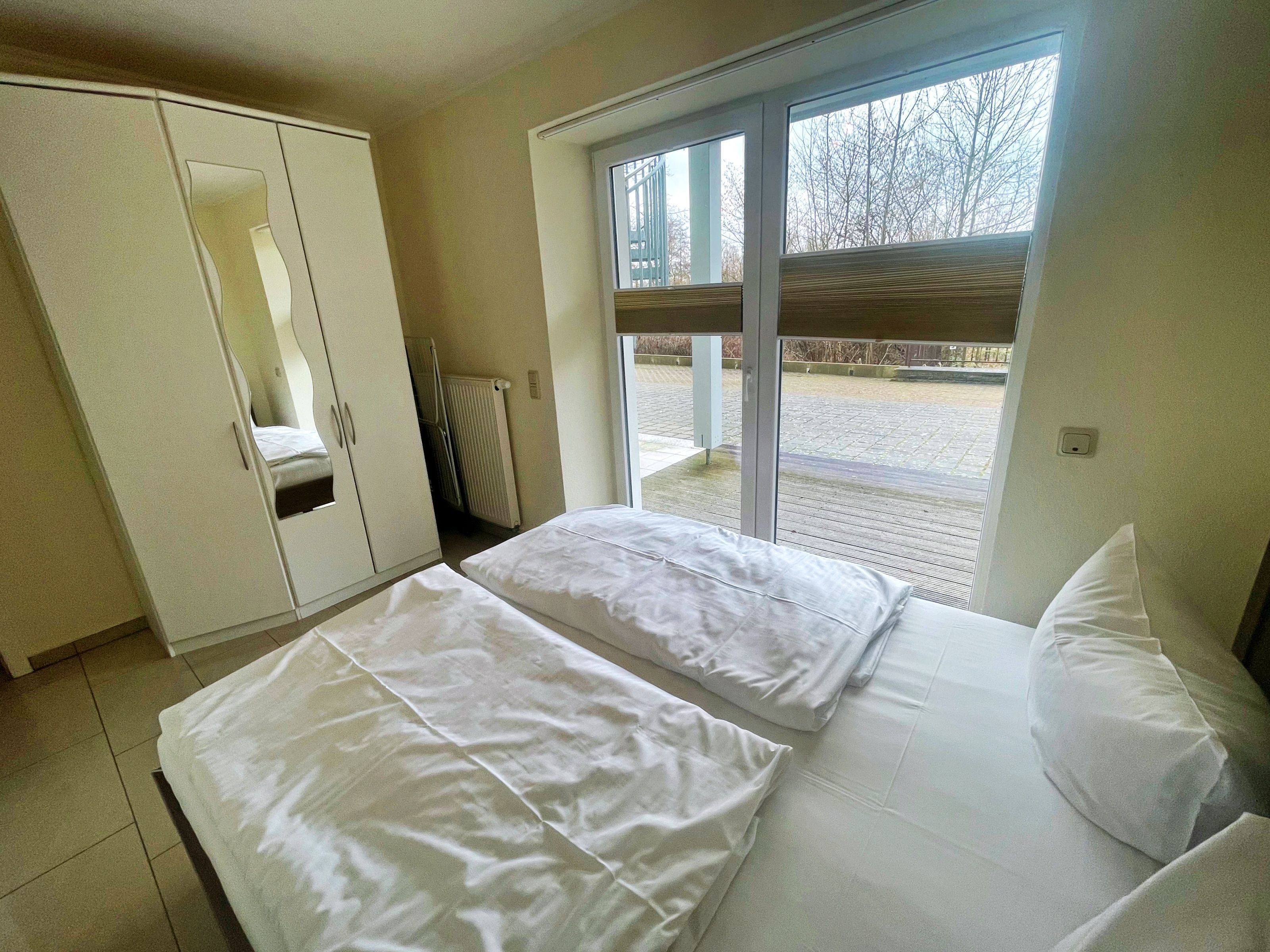 Ein Schlafzimmer mit zwei Betten, einem Kleiderschrank und einem großen Fenster mit Blick nach außen.