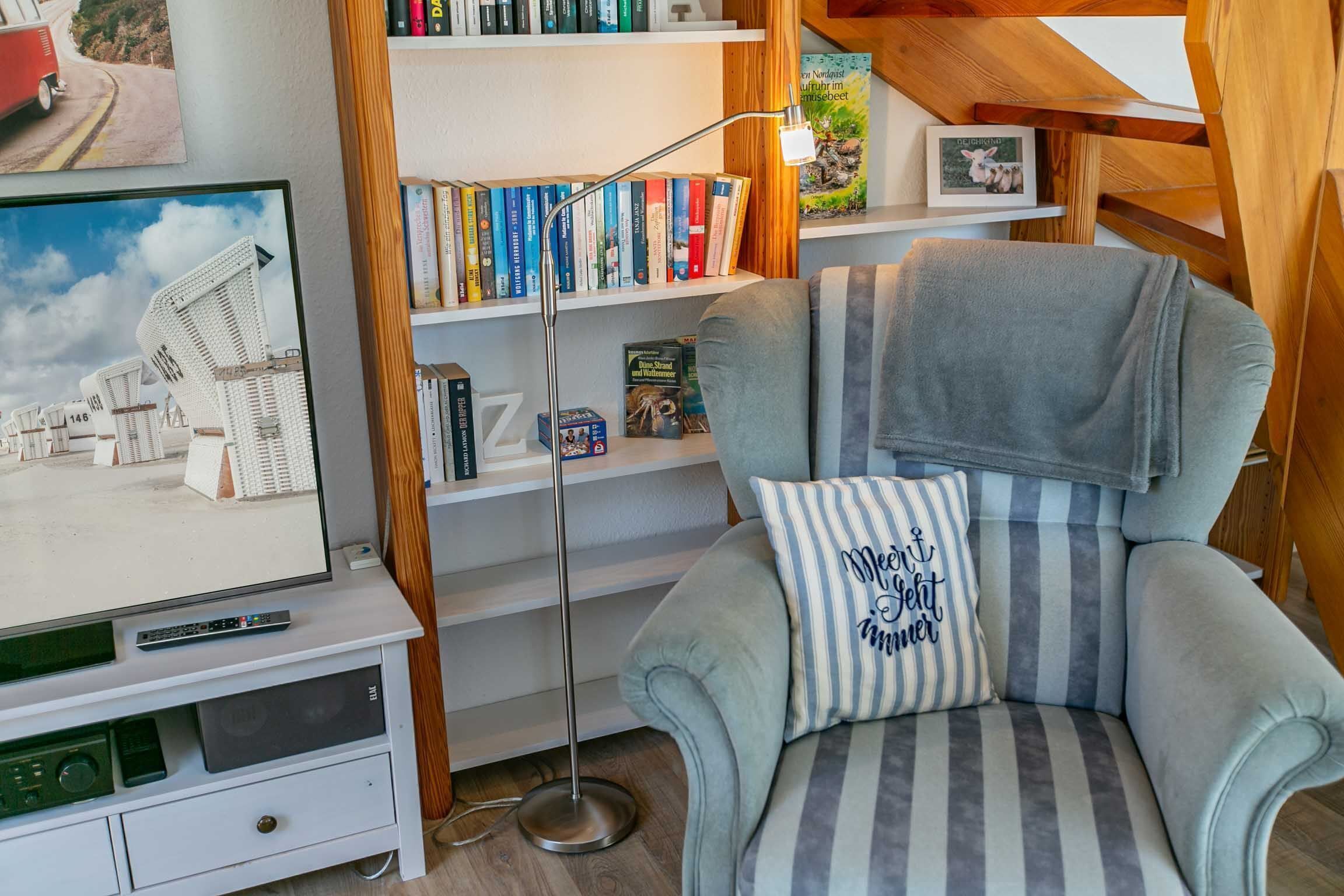 Eine gemütliche Leseecke mit gepolstertem Sessel, Bücherregal und Flachbildfernseher.