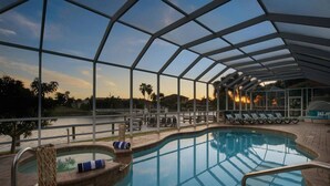 Zona de piscina con cerramiento de vidrio, sillas de descanso y vistas al atardecer.