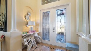 Un vestíbulo con una columna blanca, un letrero de bienvenida, un espejo y una puerta con vidrieras.