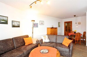 A living room with two sofas, a coffee table, and a dining area with wooden furniture.