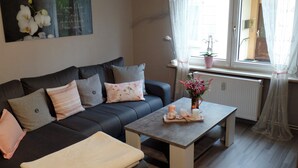 Ein modernes Wohnzimmer mit einem dunkelgrauen Sofa, einem Holztisch und einem Fenster mit leichtem Vorhang.