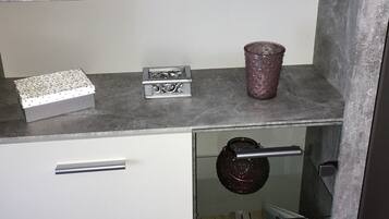 Eine Küche mit Marmorarbeitsplatte, einem weißen Schrank, einer Vitrine mit Büchern und einer dekorativen Karaffe.