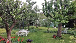 Ein Garten mit einem weißen Metalltisch und -stühlen, umgeben von Bäumen und blühenden Pflanzen.