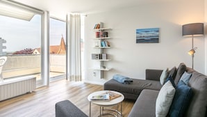 A modern living room with a grey sofa, a small round table, and a bookshelf.