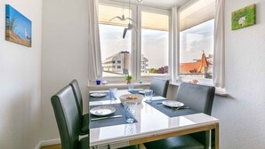 A dining area with a table set for four, chairs, a vase, and a window with a view of buildings.