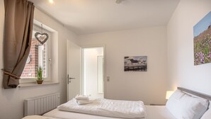 A hotel room with two beds, a window with a view of a brick building, a heart-shaped decoration, and a painting on the wall.