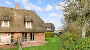 A thatched-roof house with a brick extension, a lawn, and a wooden fence.