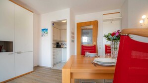 A compact kitchen with white cabinets, a wooden dining table, and a red chair. - Apartment 14 (ID 212), Germany (Sankt Peter-Ording)