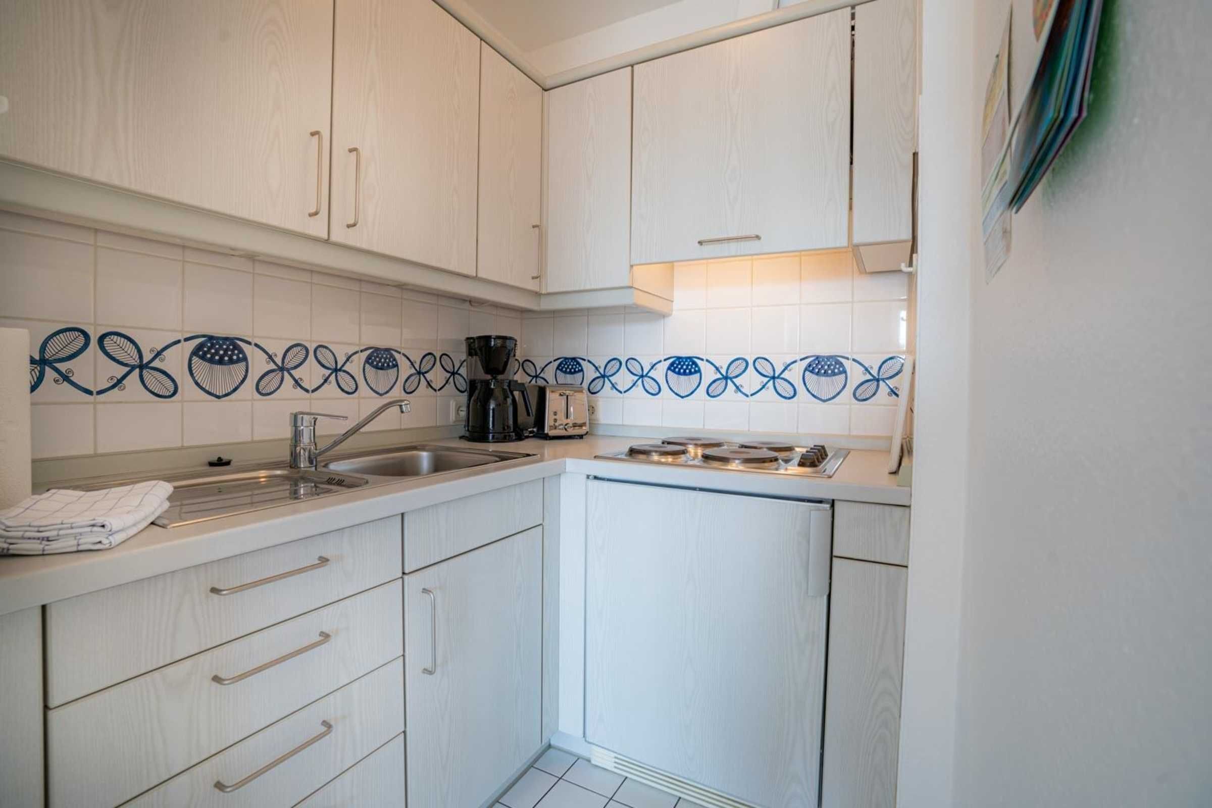 A compact kitchen with white cabinets, a stainless steel sink, and a coffee maker.