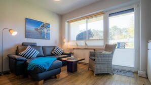 Ein gemütliches Wohnzimmer mit einer Couch, einem Korbstuhl, einem Couchtisch und einem Bild an der Wand.
