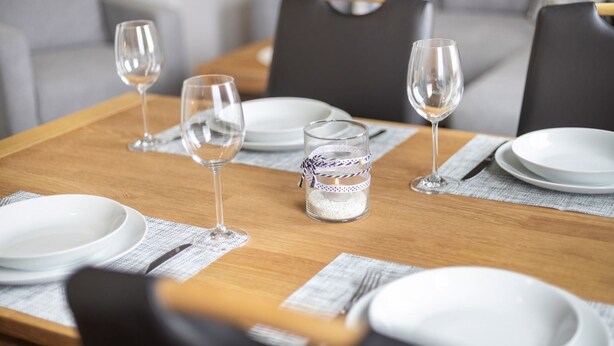 A dining table set with white plates, clear wine glasses, and a candle in a glass jar. - Apartment OG (ID 135), Germany (Sankt Peter-Ording)