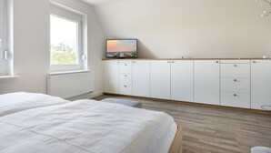 A bedroom with two beds, a large window, a TV on a cabinet, and a view of the outdoors. - Apartment OG (ID 135), Germany (Sankt Peter-Ording)