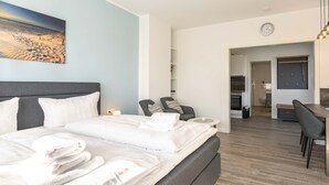 A modern hotel room with a large bed, a desk, and a dining area. - Apartment ground floor behind (ID 136) (Sankt Peter-Ording)