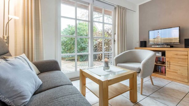 A modern living room with a sofa, a coffee table, a TV, and a bookshelf. - House section 6 Port (ID 300) (Sankt Peter-Ording)