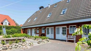 A two-story house with a tiled roof, a stone pathway, and a bench. - House section 6 Port (ID 300) (Sankt Peter-Ording)