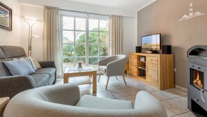 A living room with a sofa, armchair, TV, wooden cabinet, and a fireplace. - House section 6 Port (ID 300) (Sankt Peter-Ording)