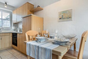A modern kitchen with wooden cabinets, a dining table set with glassware, and a painting on the wall.
