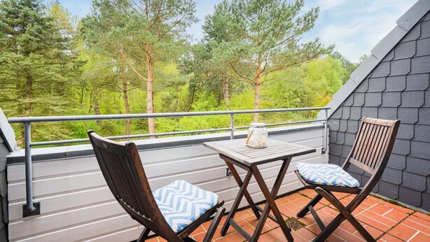 A balcony with two wooden chairs and a small table, overlooking a forested area. - Apartment OG (ID 313), Germany (Sankt Peter-Ording)