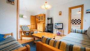 A cozy living room with a wooden sofa, striped cushions, a wooden dining table, and a television on a stand. - Apartment OG (ID 313), Germany (Sankt Peter-Ording)