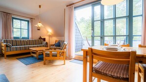 A cozy room with a sofa, chairs, a dining table, and large windows. - Apartment OG (ID 313), Germany (Sankt Peter-Ording)