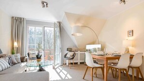 A modern living room with a glass coffee table, a sofa, and a dining area with a wooden table and chairs.