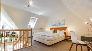 A bedroom with a bed, bedside tables, a desk, and a chair. There is a window and a painting on the wall.