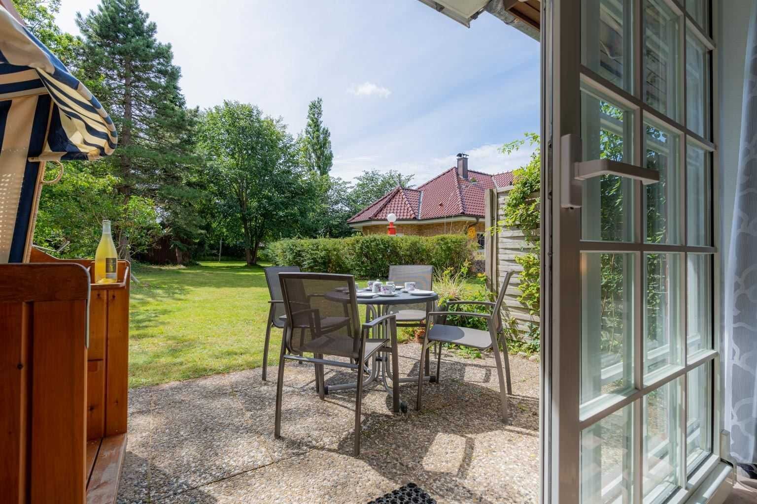 Une terrasse extérieure avec une table et des chaises, une terrasse en bois et une vue sur une maison avec un toit rouge.