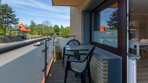 A balcony with a table and chairs, a potted plant, and a view of a building with a red roof. - Apartment 1 "Starfish" (ID 292) (Room category) - Apartment 1 "Starfish" (ID 292) (Sankt Peter-Ording)