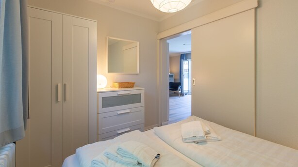 A hotel room with a bed, a dresser, a mirror, and a door leading to another room. - Apartment 1 "Starfish" (ID 292) (Room category) - Apartment 1 "Starfish" (ID 292) (Sankt Peter-Ording)