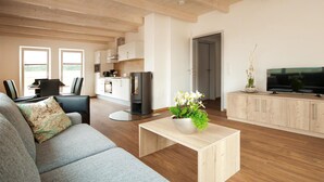 A modern living room with a sofa, a coffee table with a plant, a TV on a wooden cabinet, and a kitchen in the background. - Ferienhaus 1 Wolfschlucht (Prüm OT Walcherath)