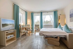 A hotel room with a bed, a desk with a chair, a television, and a window with curtains.