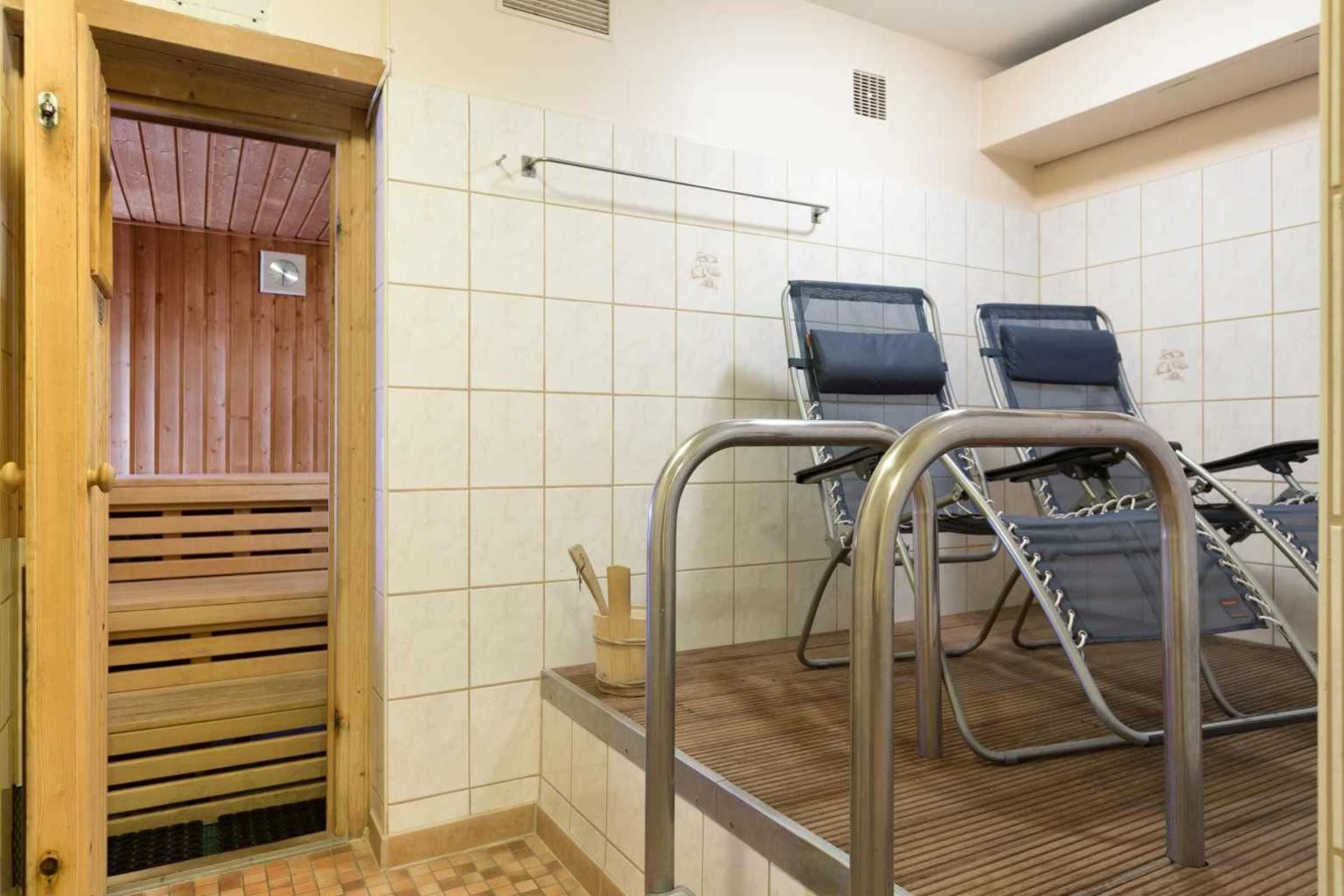 A sauna room with two reclining chairs, a wooden door, and tiled walls.