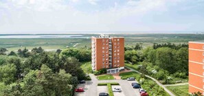 A multi-story building with a parking lot and a view of a large open area with greenery and a body of water in the background.