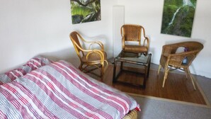 Quarto com cama, duas cadeiras de vime, uma mesinha e duas molduras na parede.
