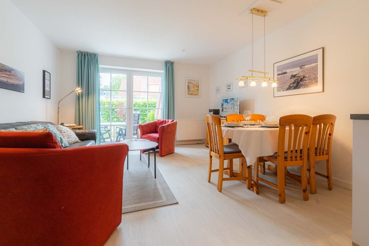 Ein modernes Wohnzimmer mit einem roten Sofa, einem Esstisch für vier Personen und einem Balkon mit Blick.