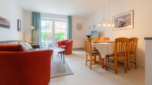 A modern living room with a red sofa, a dining table set for four, and a balcony with a view. - House part 19 (ID 032) - House Nordlys (Sankt Peter-Ording)