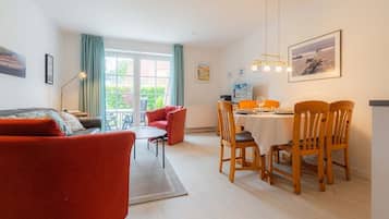Ein modernes Wohnzimmer mit einem roten Sofa, einem Esstisch für vier Personen und einem Balkon mit Blick.