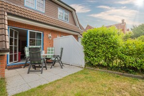 A house with a patio area featuring a table and chairs, a white fence, and a well-maintained hedge. - House part 19 (ID 032) - House Nordlys (Sankt Peter-Ording)