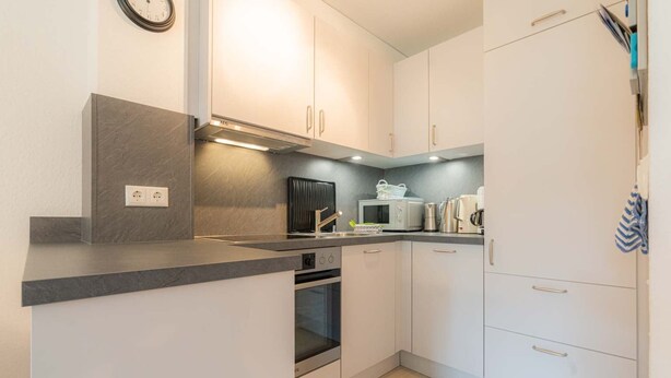 A modern kitchen with white cabinets, a built-in oven, a microwave, and a coffee maker. - House part 19 (ID 032) - House Nordlys (Sankt Peter-Ording)