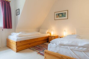 A cozy, triangular room with two wooden beds, a colorful rug, and a painting on the wall. - House part 19 (ID 032) - House Nordlys (Sankt Peter-Ording)