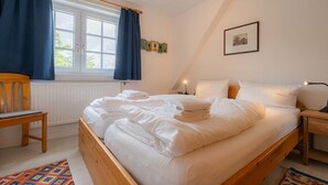 A bedroom with a wooden bed, a chair, a nightstand, and a window with curtains. - House part 19 (ID 032) - House Nordlys (Sankt Peter-Ording)