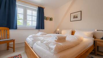Ein Schlafzimmer mit einem Holzbett, einem Stuhl, einem Nachttisch und einem Fenster mit Vorhängen.