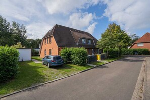 A residential house with a sloped roof, a car parked in the driveway, and a well-maintained lawn. - House part 19 (ID 032) - House Nordlys (Sankt Peter-Ording)