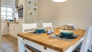 A dining area with a wooden table set for four, surrounded by white chairs. - Apartment 2 "Nordseetraum 2" (ID 059) - Haus Storchennest (Sankt Peter-Ording)