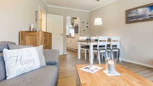 A cozy living room with a grey sofa, a wooden coffee table, and a dining area with a white table and chairs. - Apartment 2 "Nordseetraum 2" (ID 059) - Haus Storchennest (Sankt Peter-Ording)