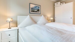 A neatly made bed with white bedding, a bedside lamp, and a framed picture on the wall. - Apartment 2 "Nordseetraum 2" (ID 059) - Haus Storchennest (Sankt Peter-Ording)