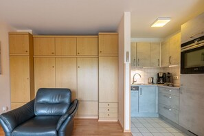 Une cuisine moderne avec des meubles en bois, un fauteuil en cuir noir et un four encastré.