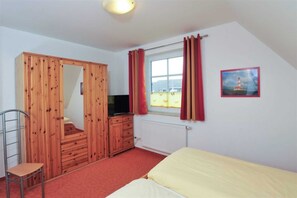 Een slaapkamer met een houten kast, een bed, een stoel, een televisie en een raam met gordijnen.